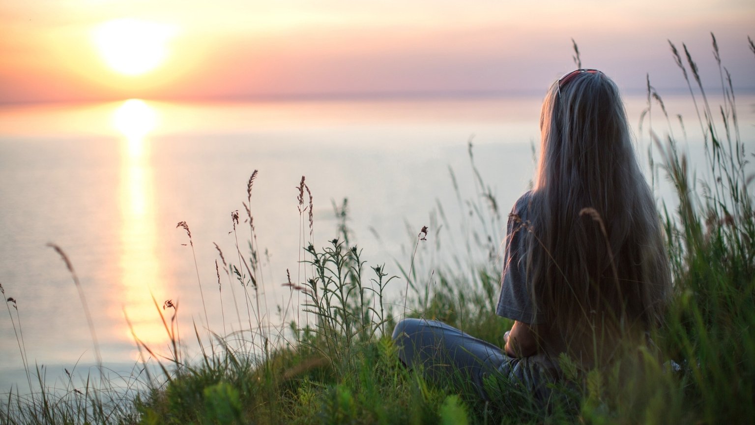 Girl sitting by the water, watching the sunset